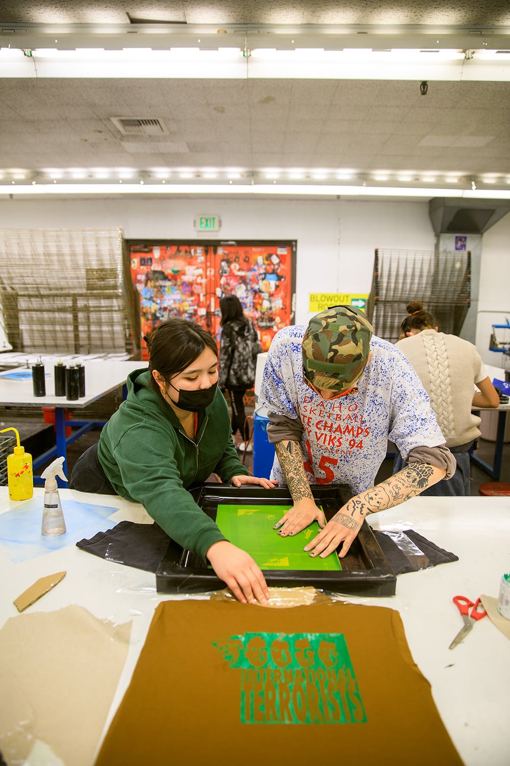 Two students work on screen print shirts.