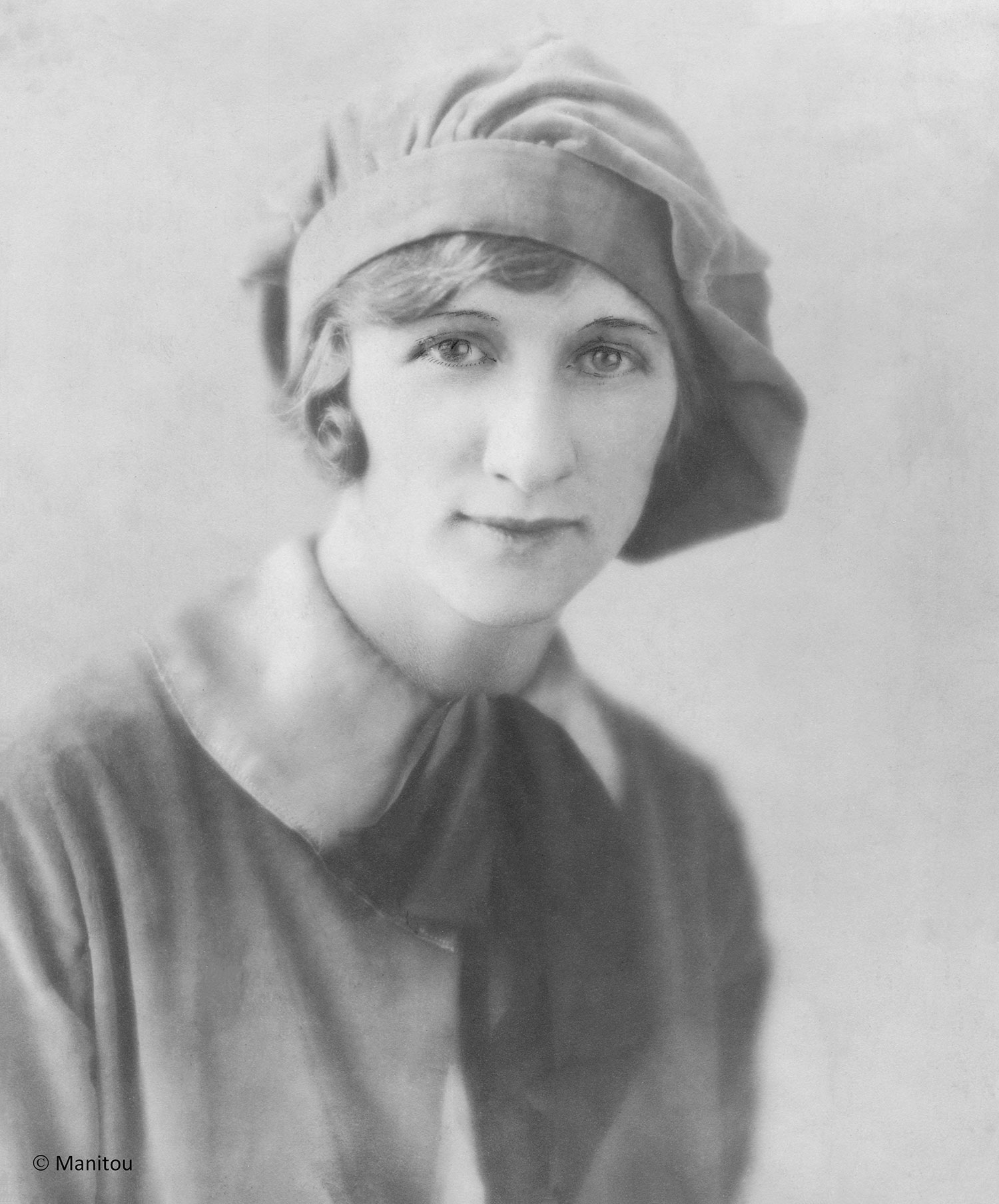 Black-and-white image of Bessie Mae Kelly, wearing a hat over short hair and a wide-collared top with a bow