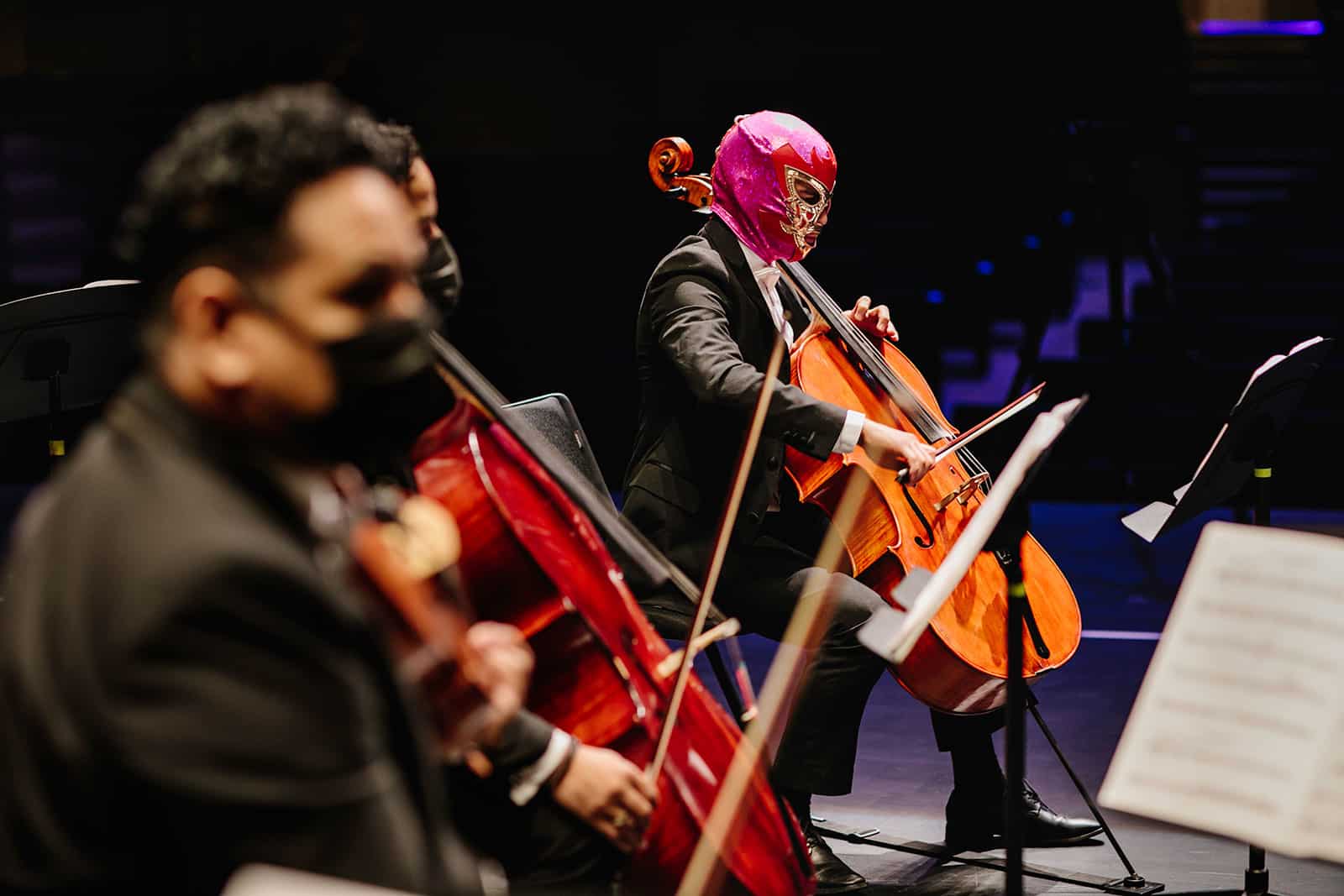 Row of cellists, one wearing a bright pink luchador mask