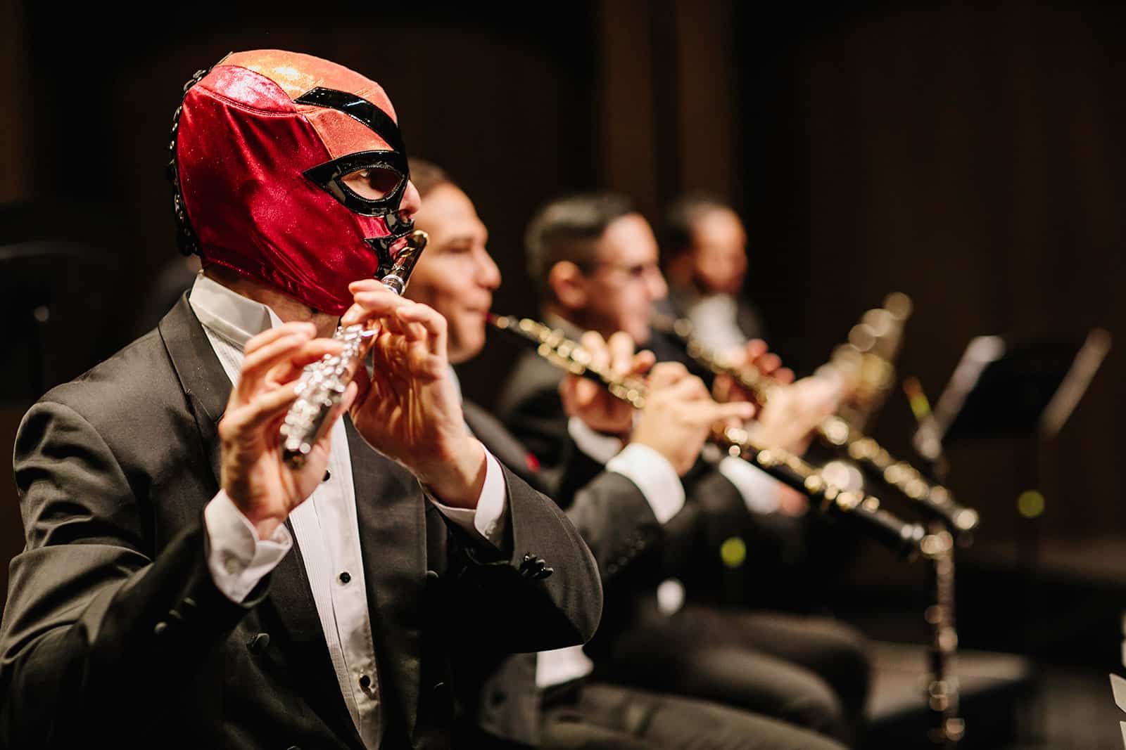Row of flautists, the closest wearing red and orange luchador mask