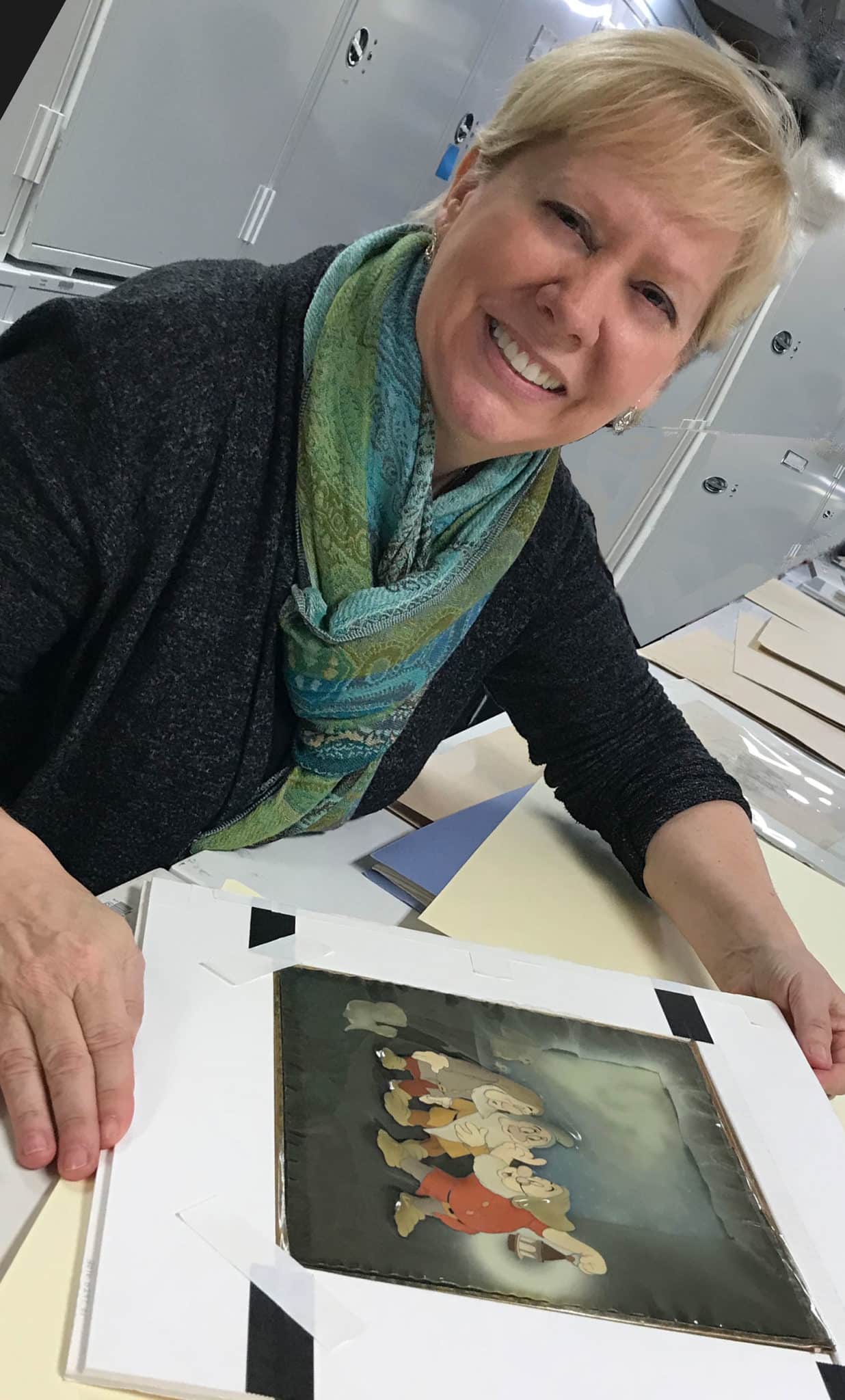 Mindy Johnson, wearing blue and green scarf, smiles while holding "Snow White" production cel