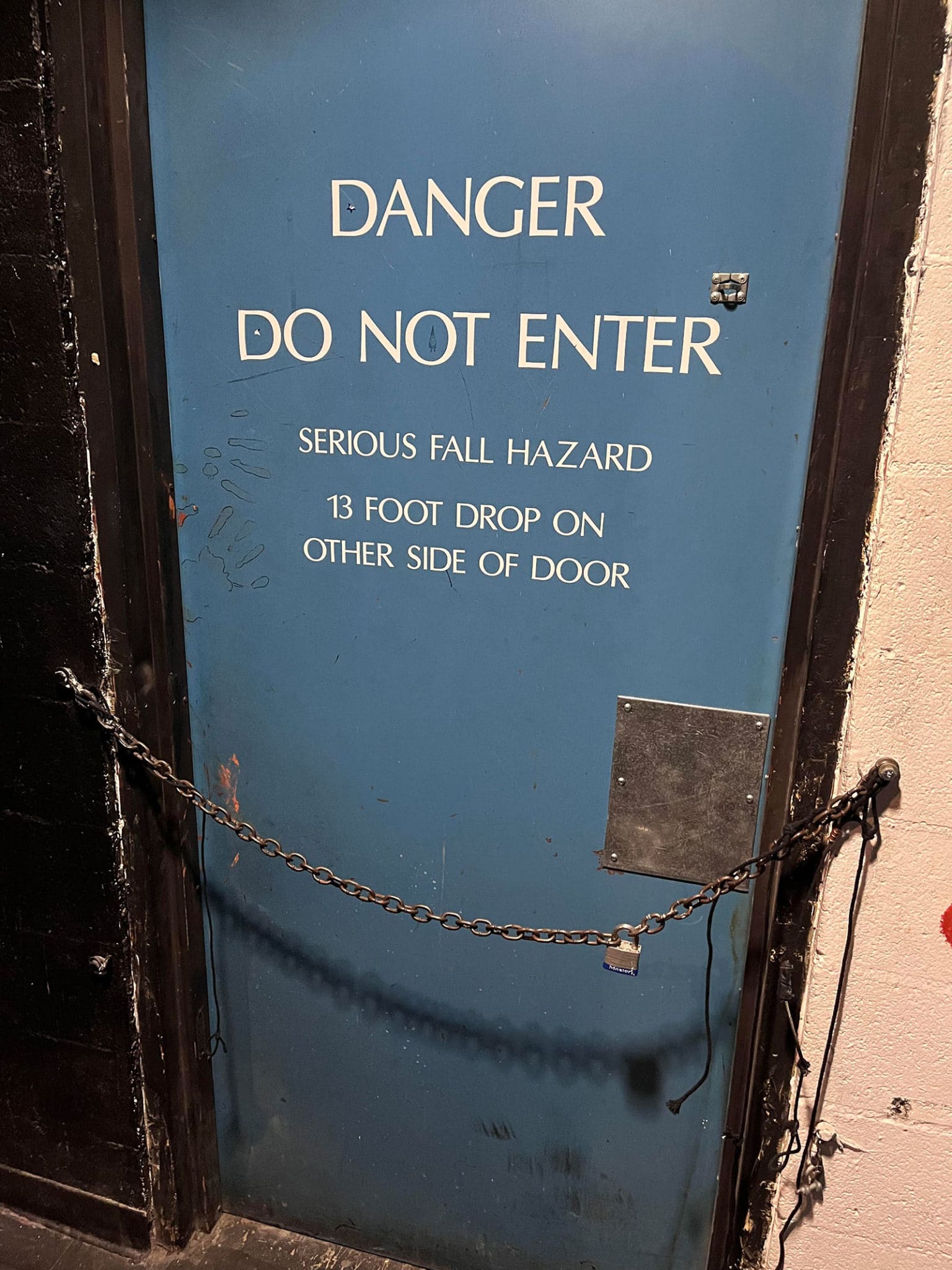 Blue door with text "Danger: Do Not Enter. Serious Fall Hazard. 13 Foot Drop on Other Side of Door"
