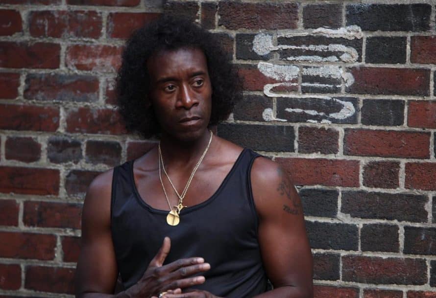 Don Cheadle as Miles Davis, in a black tank top, standing against a brick wall.