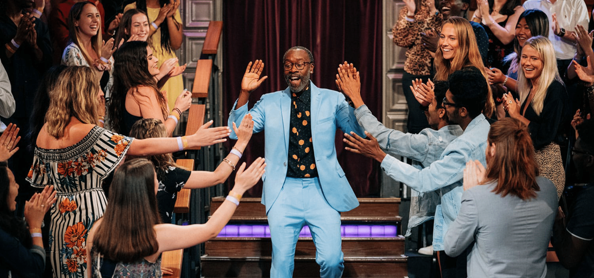 Don Cheadle in blue suit steps down stairs while high-fiving audience members