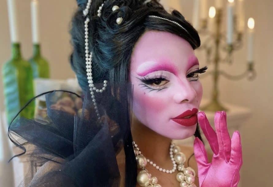 Jasmine Sugar wears pink opera gloves, a large pearl necklace, and bright pink drag makeup