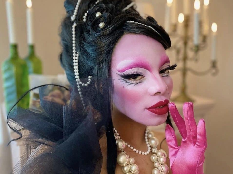 Jasmine Sugar wears pink opera gloves, a large pearl necklace, and bright pink drag makeup