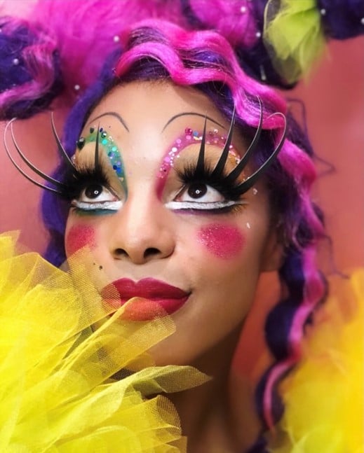 Portrait of Jasmine Sugar as Spotlight with pink and purple wig, yellow tulle sleeves, and dramatic eyelashes and makeup