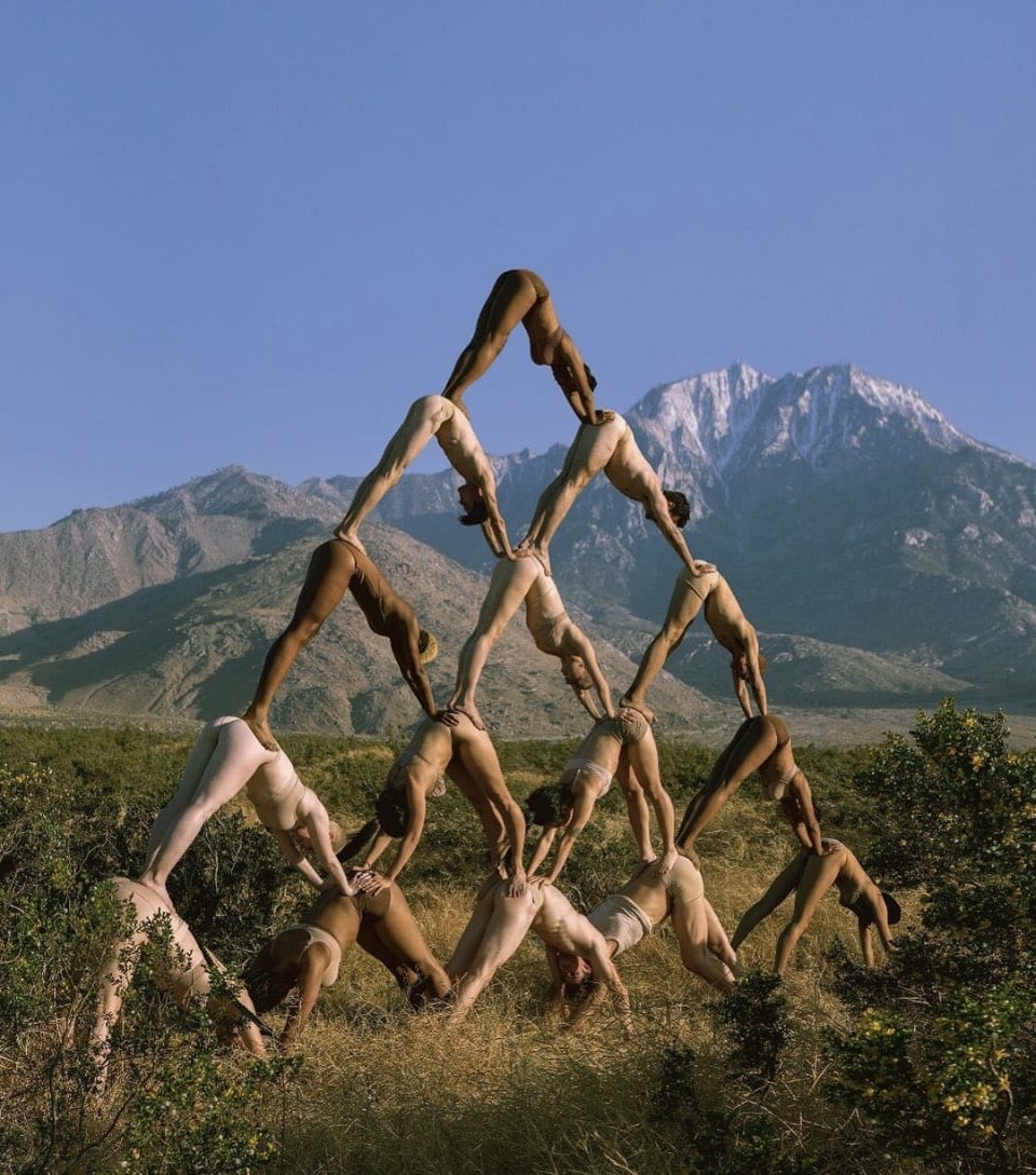 Fifteen dancers poses in a pyramid amid mountain backdrop