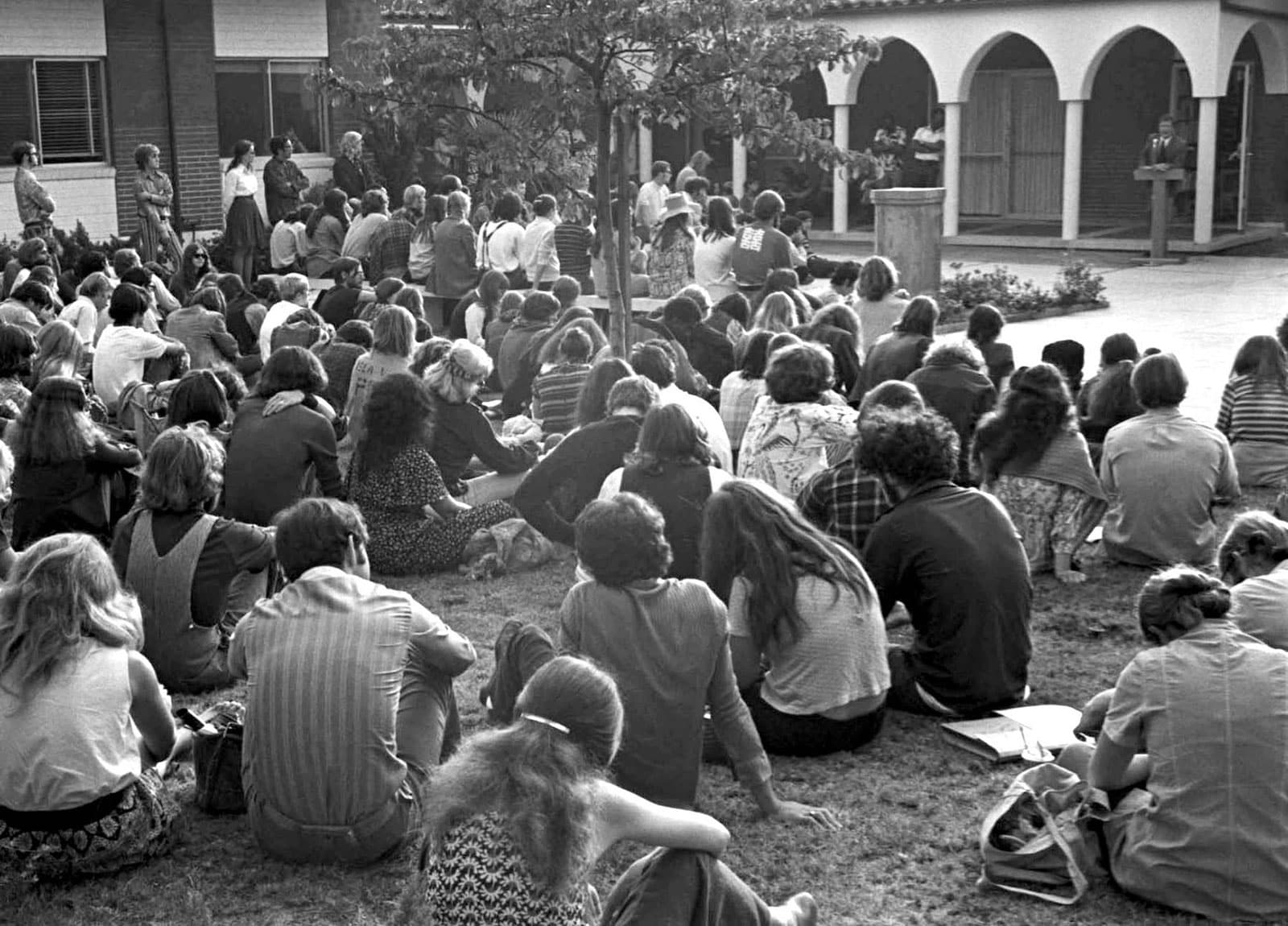 Black-and-white image of student body seated on grass