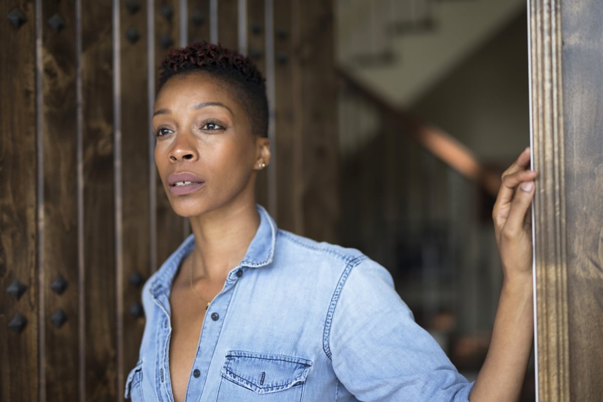 A person in a blue jean shirt looks pensively toward the right with a set of stairs in the background.