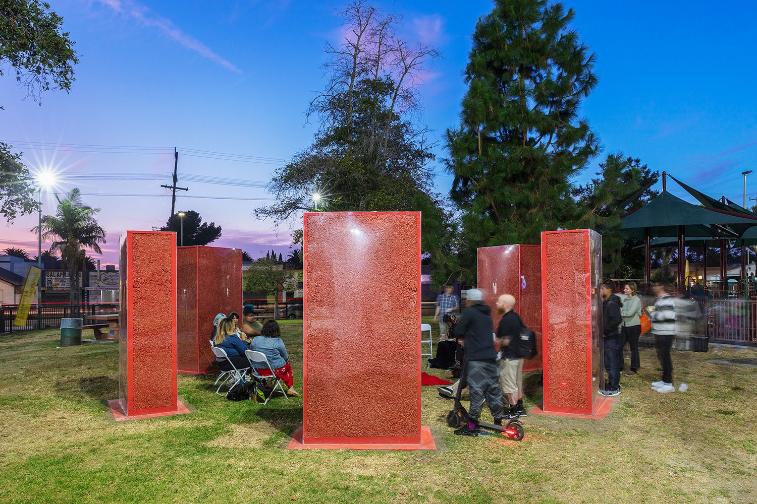 People sit and observe array of glass structures filled with Hot Cheetos arranged in circle