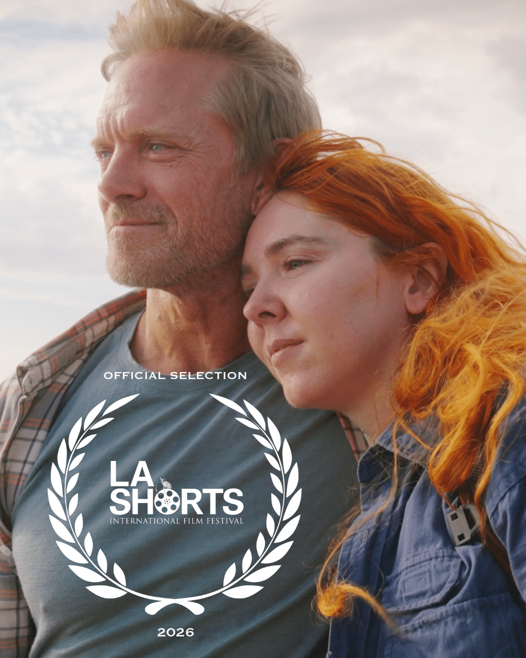 A close-up of a man and woman in a tender moment, with the man sporting blond hair and a beard and the woman having vibrant orange hair. Overlayed with "LA SHORTS" festival logo and the text "OFFICIAL SELECTION."
